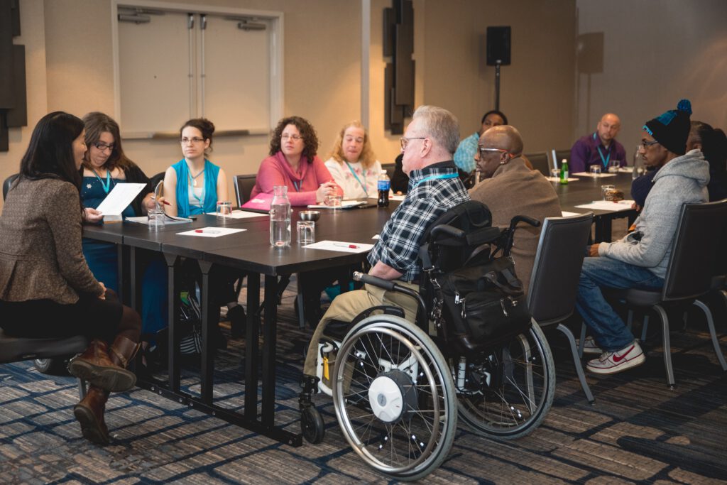 A diverse group of people sit around a conference table engaged in conversation.